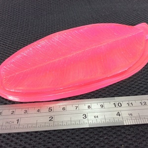 May include: A bright pink silicone mold shaped like a banana leaf. The mold is approximately 7 inches long and 2 inches wide.