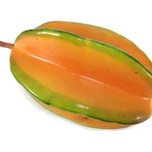 May include: A yellow star fruit with green stripes. The fruit is ripe and ready to eat.