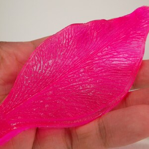 Op de afbeelding: Een felroze, plastic rozenblad met een getextureerd oppervlak. Het blad is ontworpen voor knutselen en het maken van kunstbloemen.