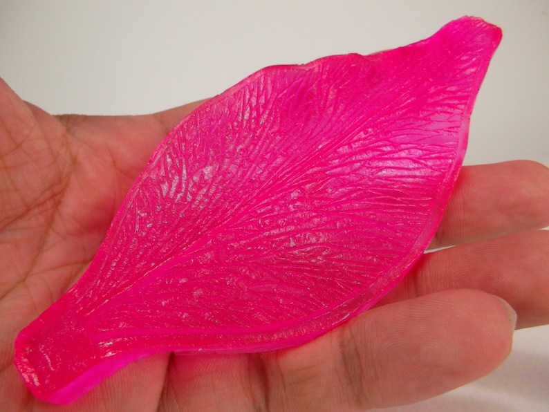 Op de afbeelding: Een felroze, plastic rozenblad met een getextureerd oppervlak. Het blad is ontworpen voor knutselen en het maken van kunstbloemen.