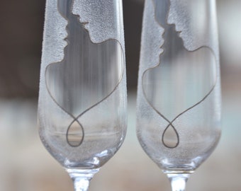May include: Two clear glass champagne flutes with a design of a couple's silhouettes intertwined in a heart shape.
