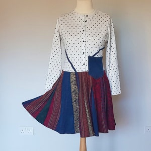 Peut inclure: Une robe blanche à pois noirs et à manches longues. La jupe est faite de différents tissus dans des tons de bleu, rouge et vert.