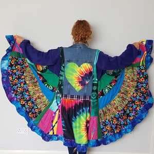 Puede incluir: Una chaqueta vaquera con un parche de corazón tie-dye y una falda de patchwork colorida adjunta. La falda tiene un dobladillo con volantes y está hecha de varias telas, incluyendo estampados florales, tie-dye y colores sólidos.
