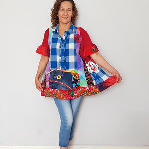 May include: A patchwork tunic featuring a mix of blue and white plaid, red fabric, denim panels, and floral patterns. The garment has short ruffled sleeves, a button-down front, and a flared hemline, paired with light blue cropped denim jeans.