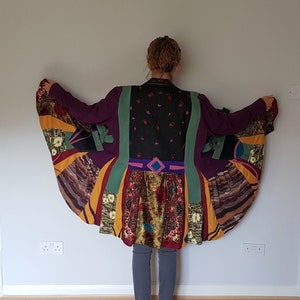 May include: A long, multi-colored, patchwork coat with a flared hem. The coat is made of different fabrics and patterns, including floral, geometric, and striped designs. The coat is a vibrant mix of colors, including purple, green, yellow, and brown.