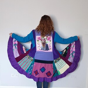 May include: A long-sleeved coat featuring a patchwork design with a central panel displaying a Yorkshire Terrier graphic surrounded by pink roses. The garment includes various fabric patterns in shades of purple, teal, and pink, with a flared hem.