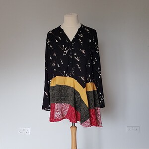 Puede incluir: Una túnica negra con estampado floral, un panel amarillo y un diseño de patchwork con estampados rojos, cachemir y piel de serpiente. La parte superior de manga larga se muestra en un maniquí de madera.