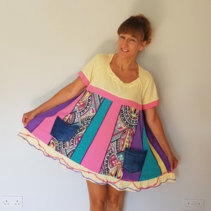 Peut inclure: Une robe en patchwork jaune, rose, violet et turquoise avec un ourlet à volants et deux poches en jean. La robe a des manches courtes et un col rond.