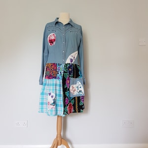 Peut inclure: Une robe chemise en jean avec une jupe en patchwork. La jupe est faite de différents tissus, dont des imprimés floraux, du plaid et du velours. La robe a un devant boutonné et des manches longues.