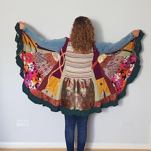 Puede incluir: Chaqueta patchwork colorida con una parte superior de mezclilla y una variedad de telas estampadas. La chaqueta presenta diseños florales, geométricos y a rayas en tonos de rosa, naranja, verde y marrón. La chaqueta tiene un ribete verde con volantes.