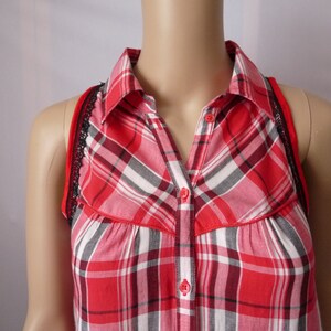 May include: Red and black plaid sleeveless shirt with a button-up collar and black lace trim.