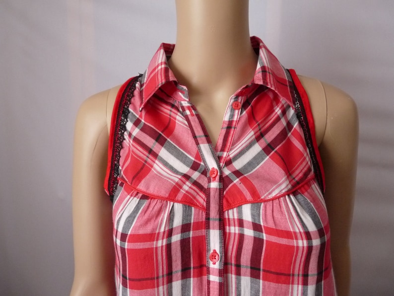 May include: Red and black plaid sleeveless shirt with a button-up collar and black lace trim.