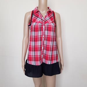 May include: A red and white plaid sleeveless shirt with a black ruffle trim. The shirt has a button-up front and a collared neckline.
