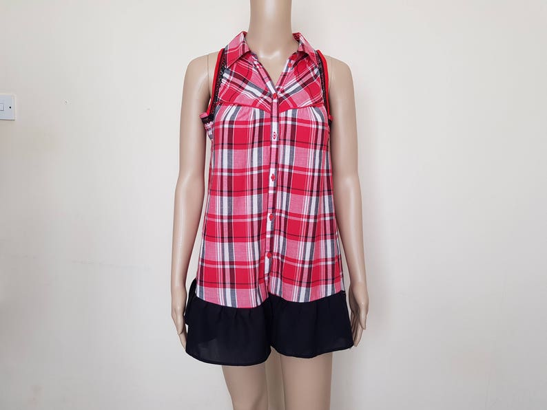 May include: A red and white plaid sleeveless shirt with a black ruffle trim. The shirt has a button-up front and a collared neckline.