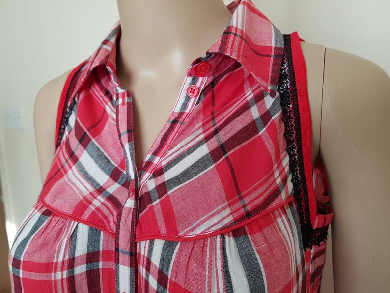 May include: Red and black plaid sleeveless shirt with a button-up collar and black lace trim on the straps.