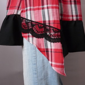 May include: A red and black plaid shirt with black lace trim and a black fabric panel on the bottom. The shirt is asymmetrical and has a pointed hem.