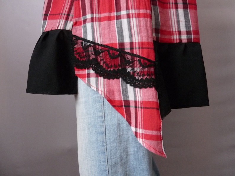 May include: A red and black plaid shirt with black lace trim and a black fabric panel on the bottom. The shirt is asymmetrical and has a pointed hem.