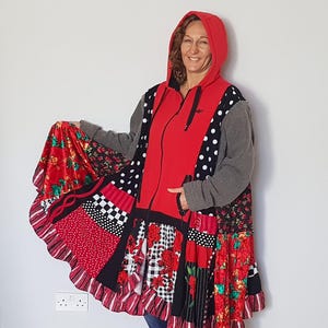 Könnte beinhalten: Eine rote Kapuzenjacke mit schwarzem Reißverschluss und grauen Ärmeln. Die Jacke hat ein Patchwork-Design mit Blumen-, Polka-Dot- und Schachbrettmustern in Rot, Schwarz und Weiß. Der untere Saum hat einen gerüschten Rand.