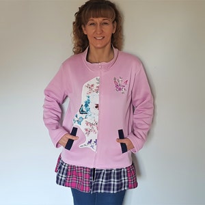 May include: A pale pink zip-up jacket with a floral and butterfly pattern on the front. The jacket has a contrasting plaid and pink skirt-like bottom. Features two navy blue pockets and floral embroidery on the upper right chest.
