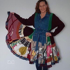 Peut inclure: Robe patchwork avec un corsage en jean, une bordure verte et un pull bordeaux. La jupe présente une variété de tissus à motifs dans les tons de rouge, bleu et jaune. La robe a une ceinture et un ourlet à volants.
