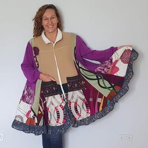 May include: A vibrant patchwork coat with a beige front, purple sleeves, and a white collar. The coat has a zip closure and two large pockets with decorative embroidery. The skirt section is a mix of patterned fabrics in various colours, with a ruffled hem.