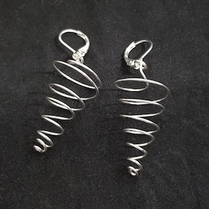 May include: A pair of silver spiral earrings. The earrings are made from a single, continuous piece of wire that is twisted into a spiral shape. The earrings are long and dangle from the ear.