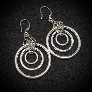 Puede incluir: Un par de pendientes de plata con tres círculos concéntricos. Los pendientes tienen un diseño simple y elegante.