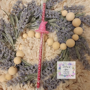 May include: A red and white polka dot straw with a pink witch hat topper. The straw is packaged in clear plastic. The straw is surrounded by lavender and wooden beads.