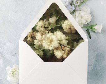 May include: A white envelope with a floral painting peeking through the opening, surrounded by white, purple, and blue flowers. The background is a light blue, textured surface, creating a soft, artistic composition.