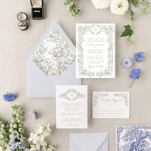 May include: A wedding invitation suite with a floral design. The invitation features a wreath of watercolor flowers and greenery with the couple's names and wedding details. The RSVP card features a similar floral design with a gold script font. The envelope liner features a floral pattern.