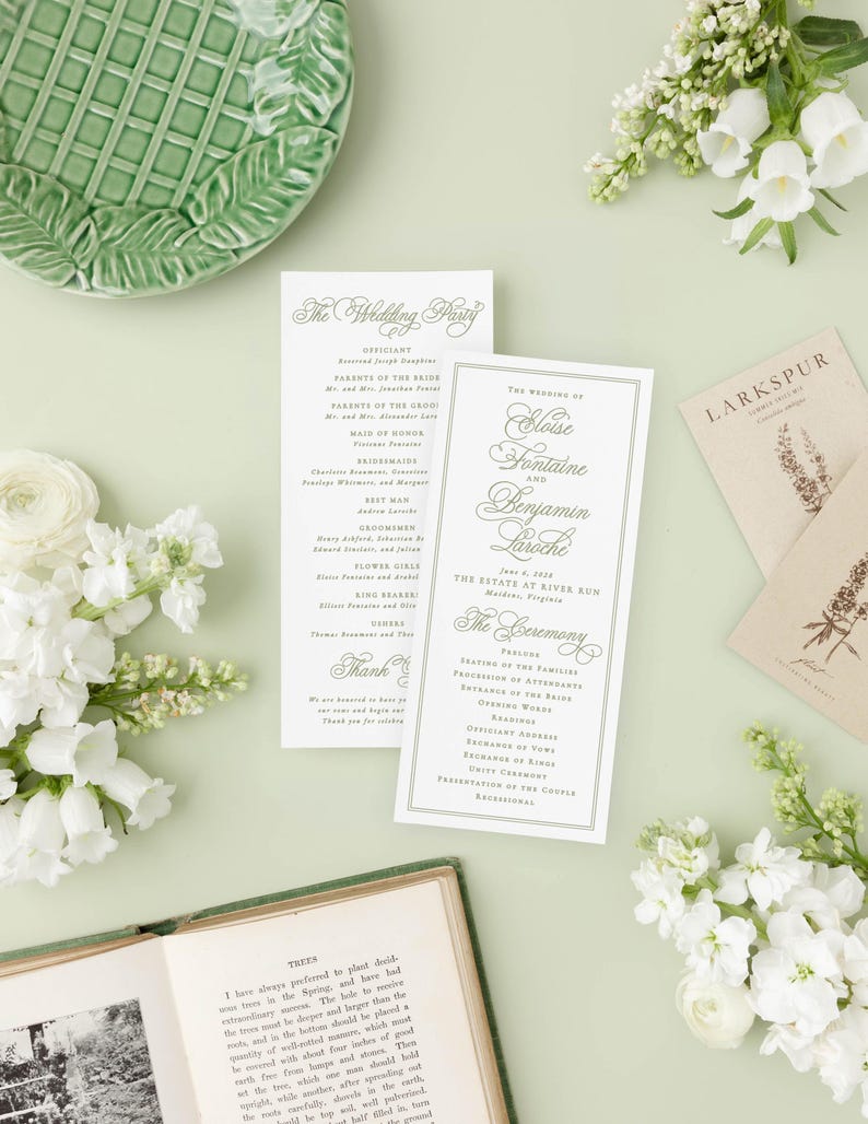 a wedding invitation with elegant calligraphy, surrounded by white flowers, a green plate, and a book.