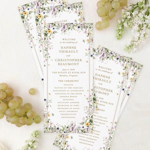 a set of wedding invitations with a floral design, placed on a white background alongside some grapes and flowers.