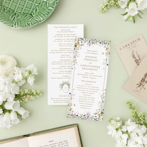 a wedding invitation with a floral design, surrounded by various wedding-related items such as a green plate, white flowers, and a book.