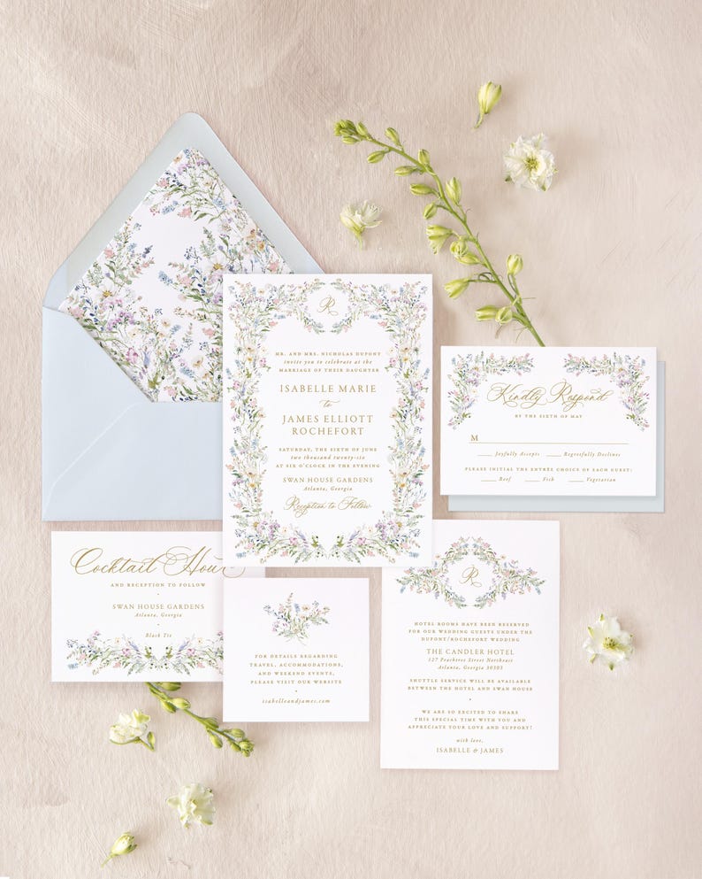 May include: A floral wedding invitation suite with a blue envelope, a white invitation card with a floral border and gold lettering, a white RSVP card with a floral border, and two white cards with floral borders and details about the cocktail hour and hotel accommodations.