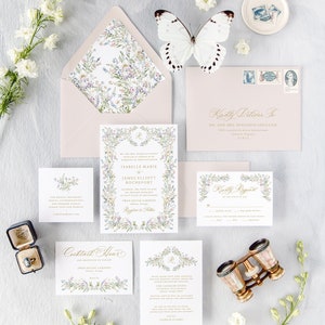 May include: A wedding invitation suite with a floral theme. The invitation features a watercolor illustration of a wreath of flowers and leaves, with the couple's names and wedding date in gold lettering. The RSVP card features a similar floral design, with a space for guests to indicate their attendance. The invitation is accompanied by a pink envelope with a floral pattern.