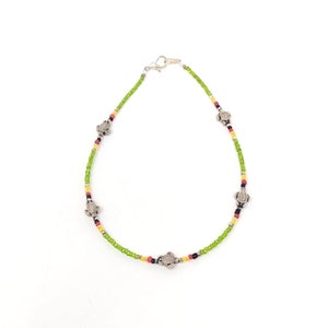 May include: A green beaded anklet with silver turtle charms. The anklet has red, yellow, and black beads.