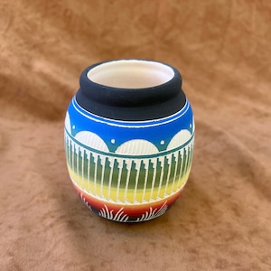 May include: A small, hand-painted ceramic pot with a geometric design in shades of blue, green, yellow, orange, and red. The pot has a black rim and a white interior.