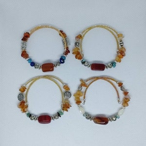 Op de afbeelding: Vier armbanden met bruine en oranje kralen, zilveren accenten en een rode rechthoekige steen in het midden van elke armband.
