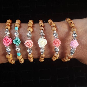 May include: Five wooden bead bracelets with silver accents and flower charms. The charms are in pink, white, turquoise, and coral.