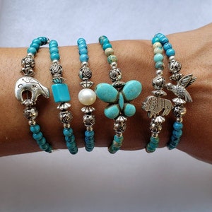 May include: Five turquoise and silver beaded bracelets with different charms. The charms include a butterfly, a bird, a buffalo, a turquoise stone, and a pearl.