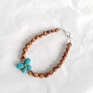 May include: A brown wooden bead bracelet with a turquoise butterfly charm. The bracelet has a silver clasp.