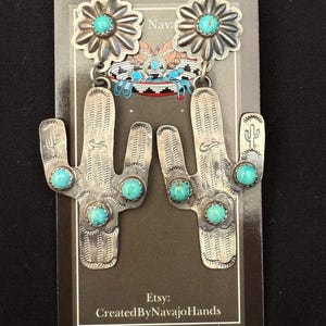 May include: Silver earrings with a daisy design and turquoise stones. The lower part of the earrings are shaped like cacti. The earrings are displayed on a black background with the text "Etsy: Created By Navajo Hands."
