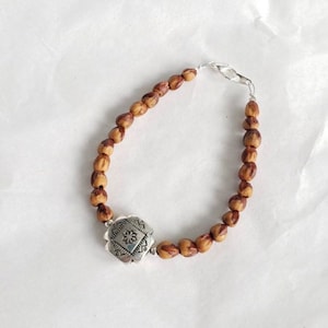 May include: A brown wooden bead bracelet with a silver charm featuring a geometric design.