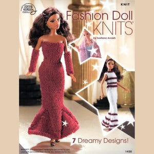 Peut inclure: Une couverture de livre présentant une poupée de mode portant une robe rouge tricotée et une poupée portant une robe tricotée rayée blanche et rouge. Le titre du livre est "Fashion Doll Knits" par Svetlana Avrakh. La couverture du livre présente également le texte "7 Dreamy Designs!" et "KNIT".