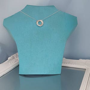 May include: A silver necklace with a five-ring pendant on a blue mannequin.
