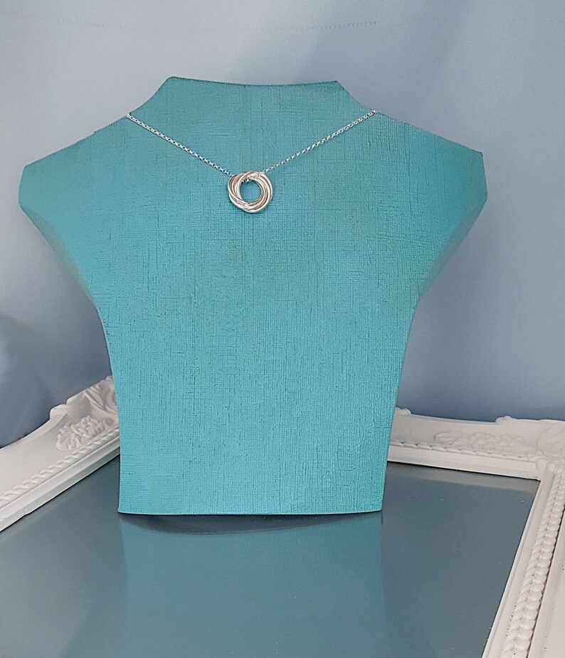 May include: A silver necklace with a five-ring pendant on a blue mannequin.