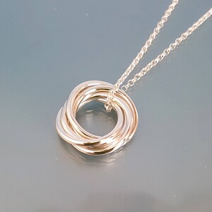 May include: A silver necklace with a pendant made of five interlocking rings.