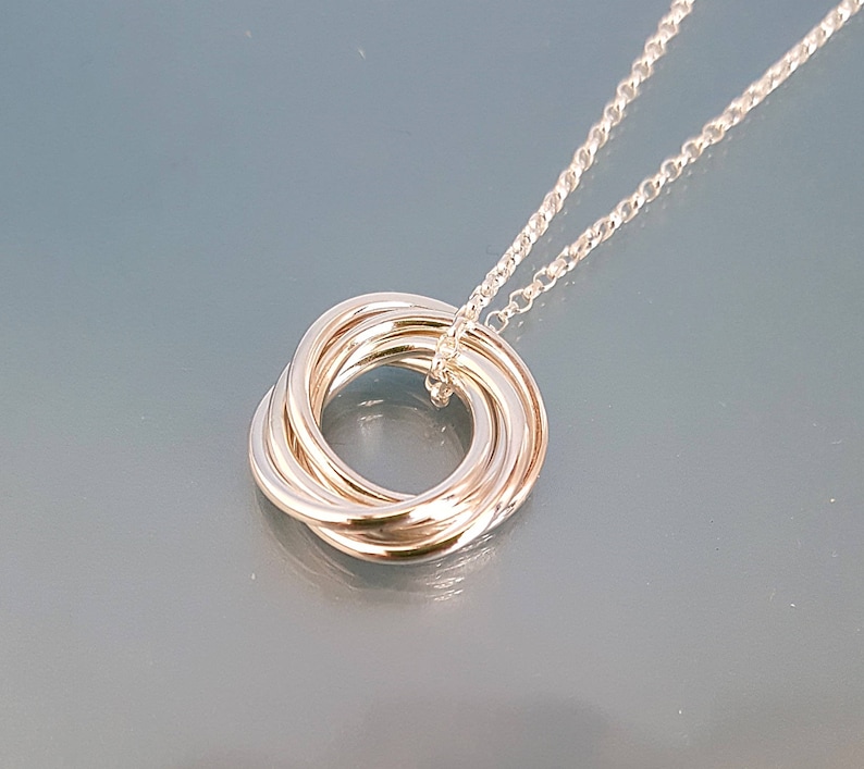 May include: A silver necklace with a pendant made of five interlocking rings.