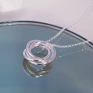 May include: A silver necklace with a pendant made of multiple interlocking rings. The chain is a delicate, silver chain.