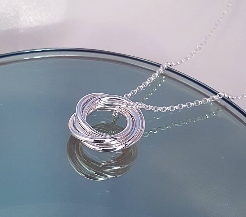 May include: A silver necklace with a pendant made of multiple interlocking rings. The chain is a delicate, silver chain.